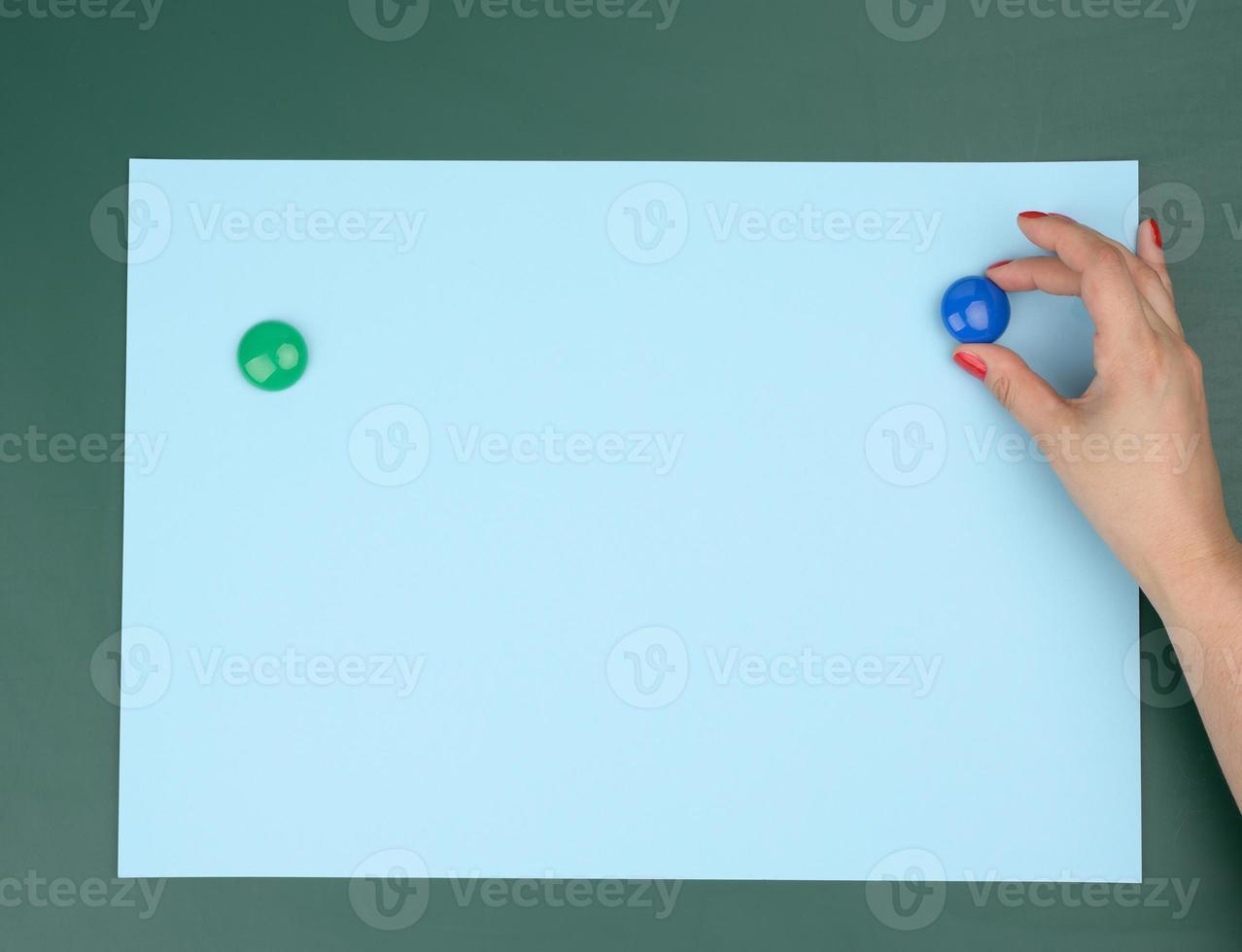 two female hands fix a blue blank sheet of paper on a magnetic board photo