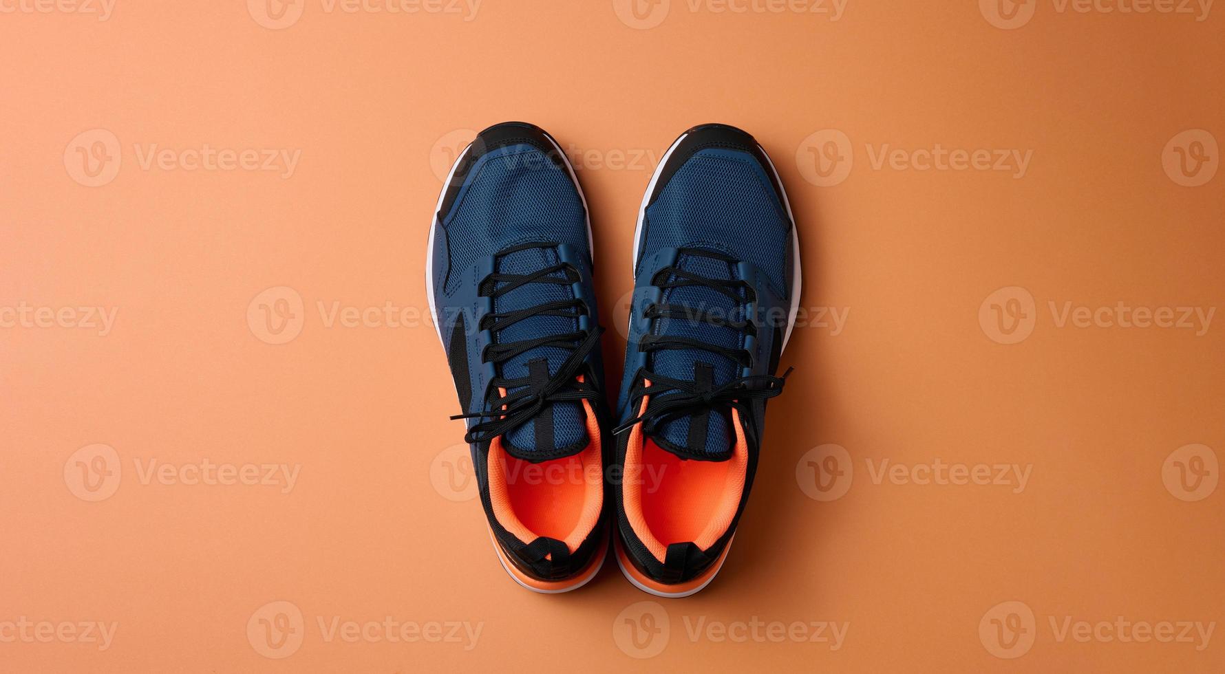 pair of blue textile sneakers on orange background, top view photo