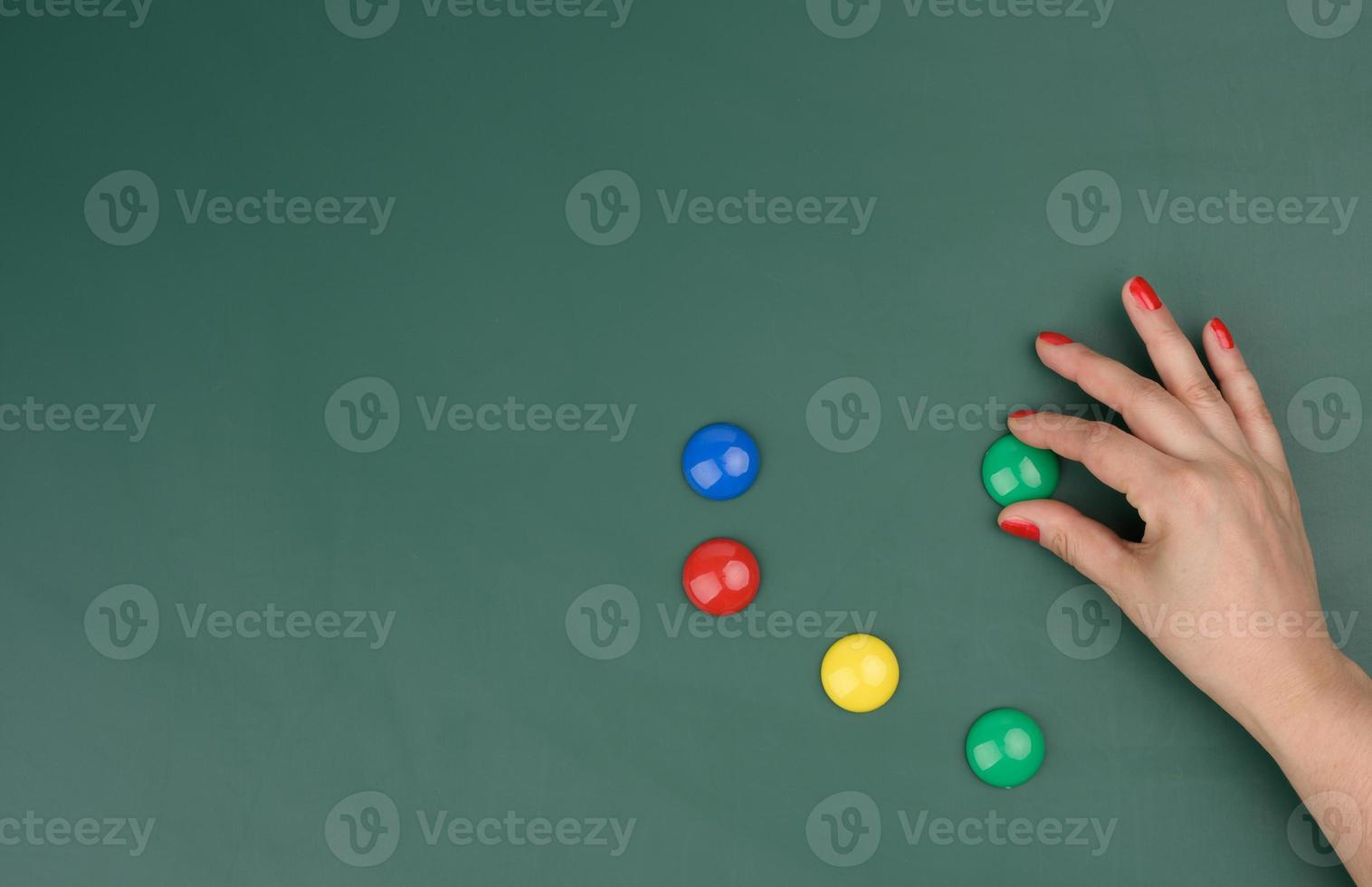 female hand attaches multi-colored magnets to a green board photo