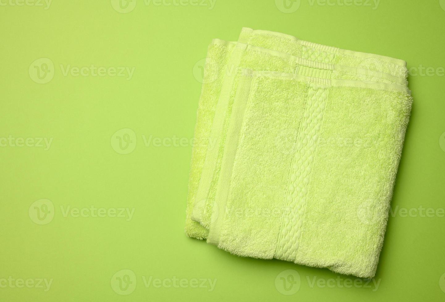 folded bath terry green towel on a green background, top view photo