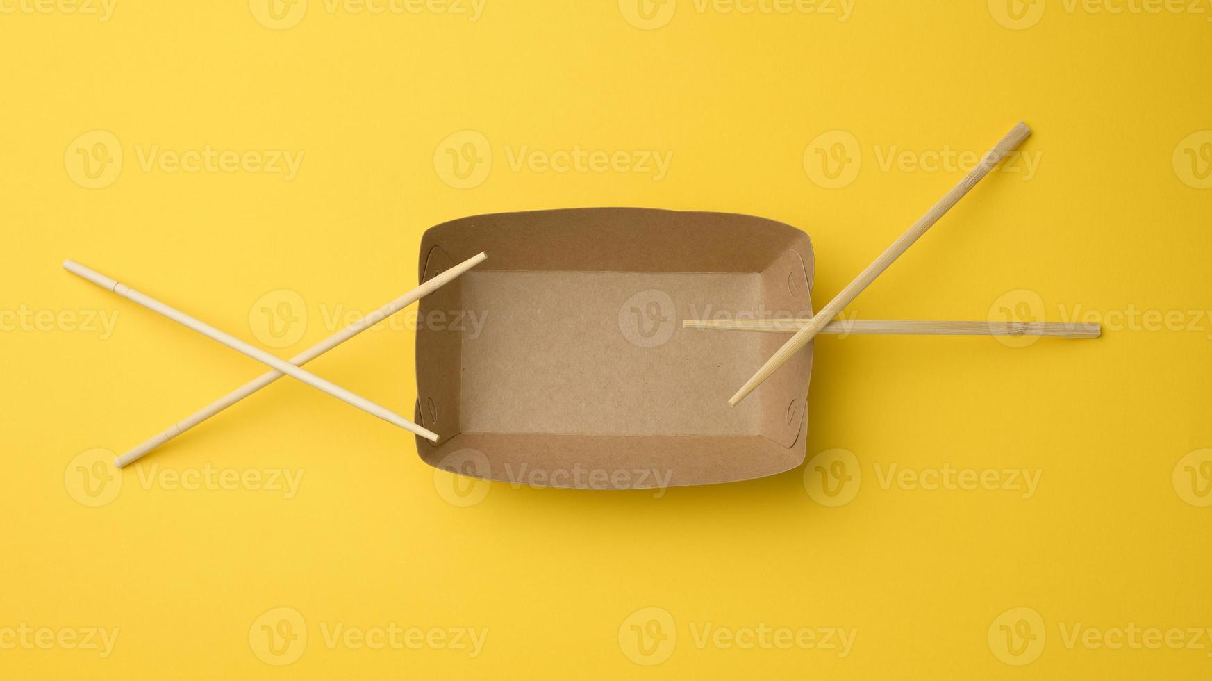 empty brown paper plate and wooden chopsticks on a yellow background, top view. Disposable tableware photo