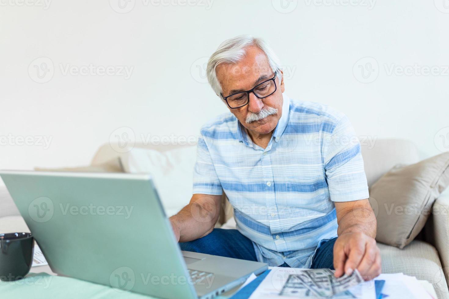 Old confident clever concentrated grandpa is checking his calculations sitting in front of monitor at office. Elderly man sitting by the table and managing his home finances. photo