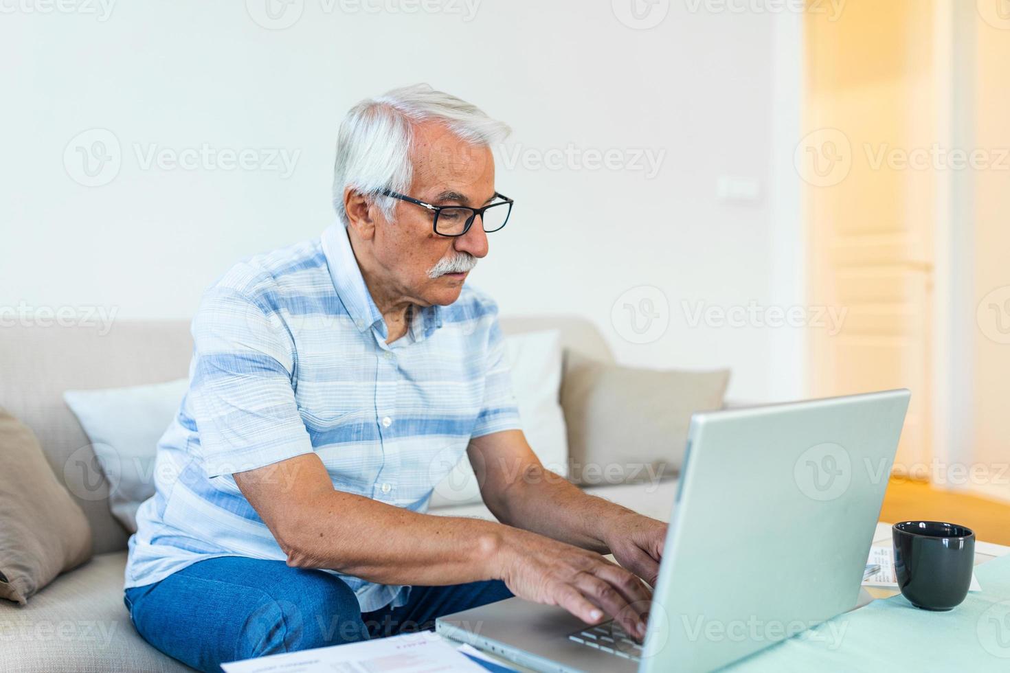 Mature businessman sit on sofa working on computer wireless device using e-banking application paying bills online, typing e-mail solve issues distantly, older generation and modern tech usage concept photo