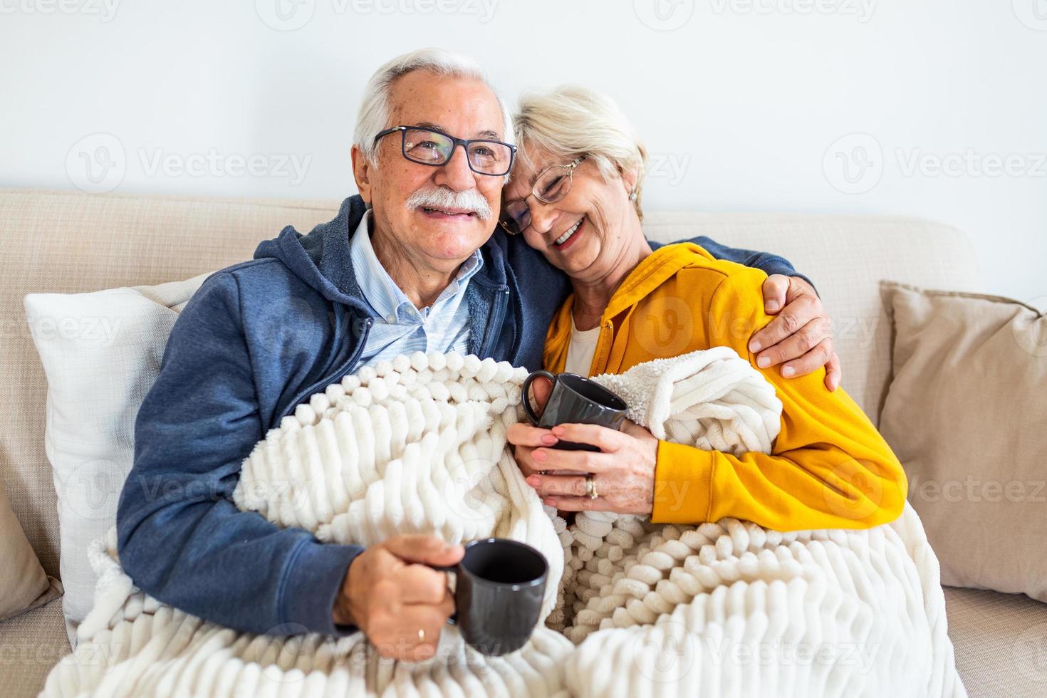 Happy old couple sitting on the sofa. Feeling cozy,drinking coffee or tea photo