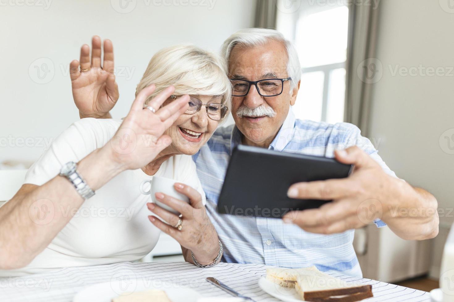 Senior couple is talking online via video connection on tablet. Having nice time withfriends and family via video call.Holding their hands together photo