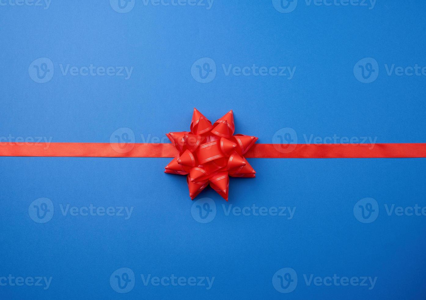 red silk ribbon and a large knotted bow on a blue background photo