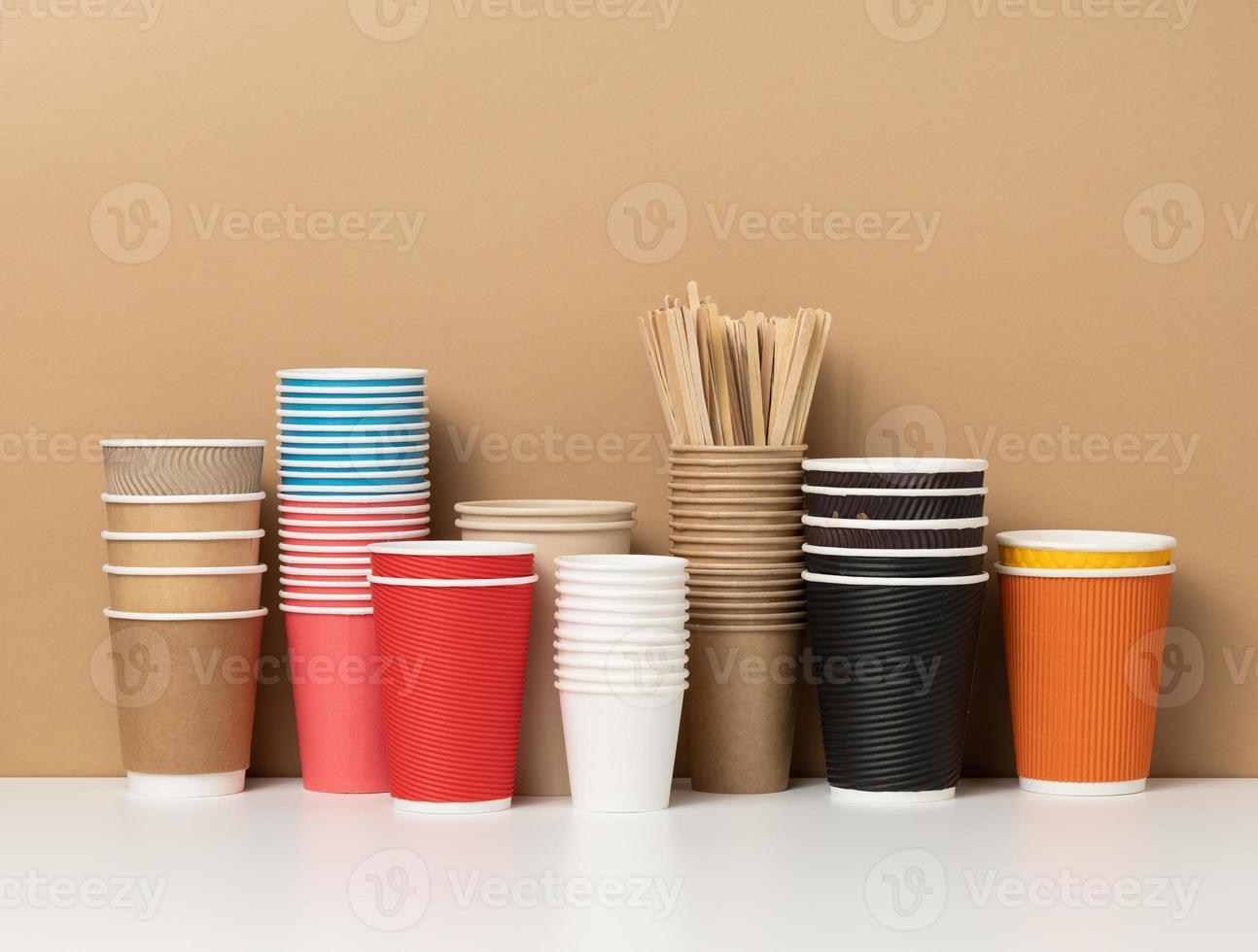 stacks of assorted disposable paper cups for drinks, coffee and tea on a white table. Takeaway beverage container photo