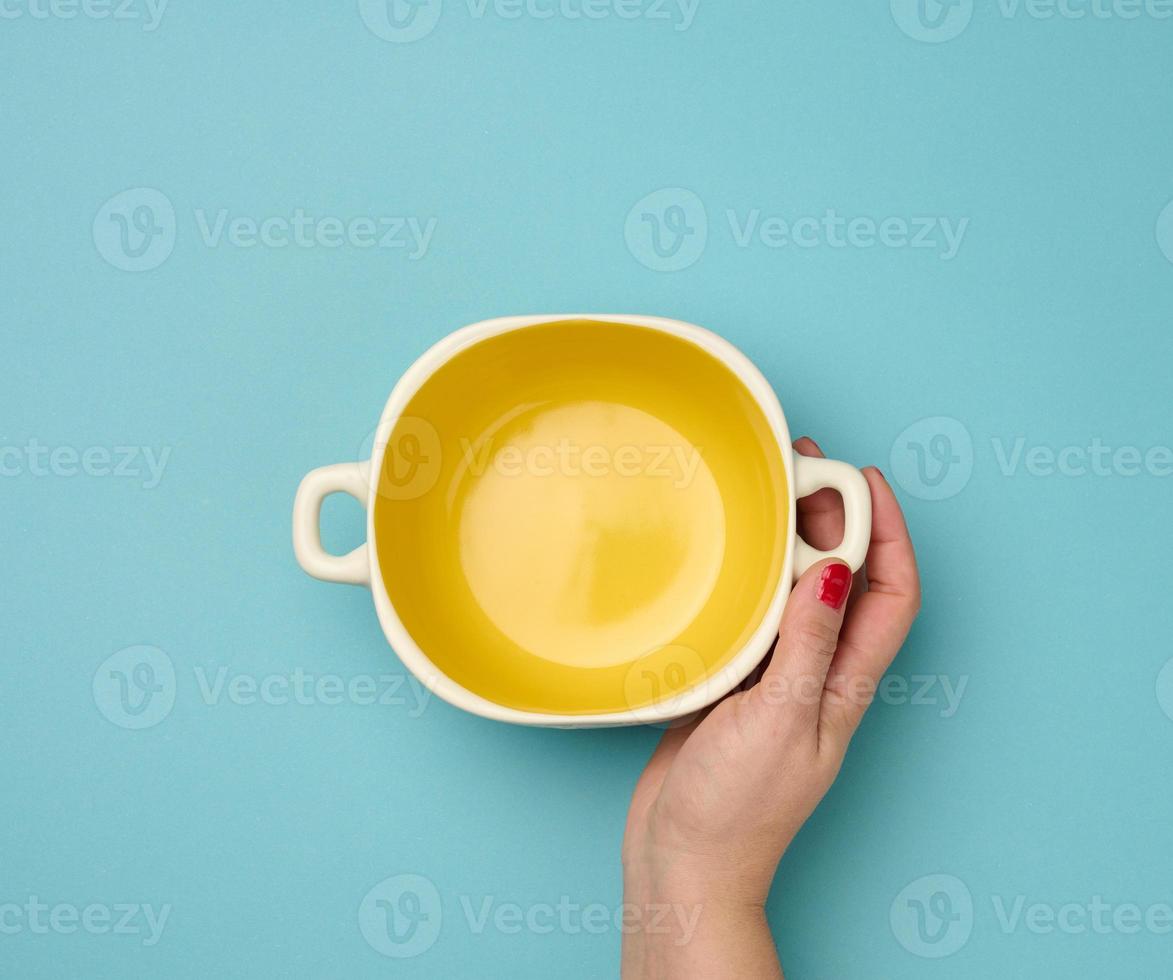 female hand holding an empty round plate with ears on a blue background, top view photo