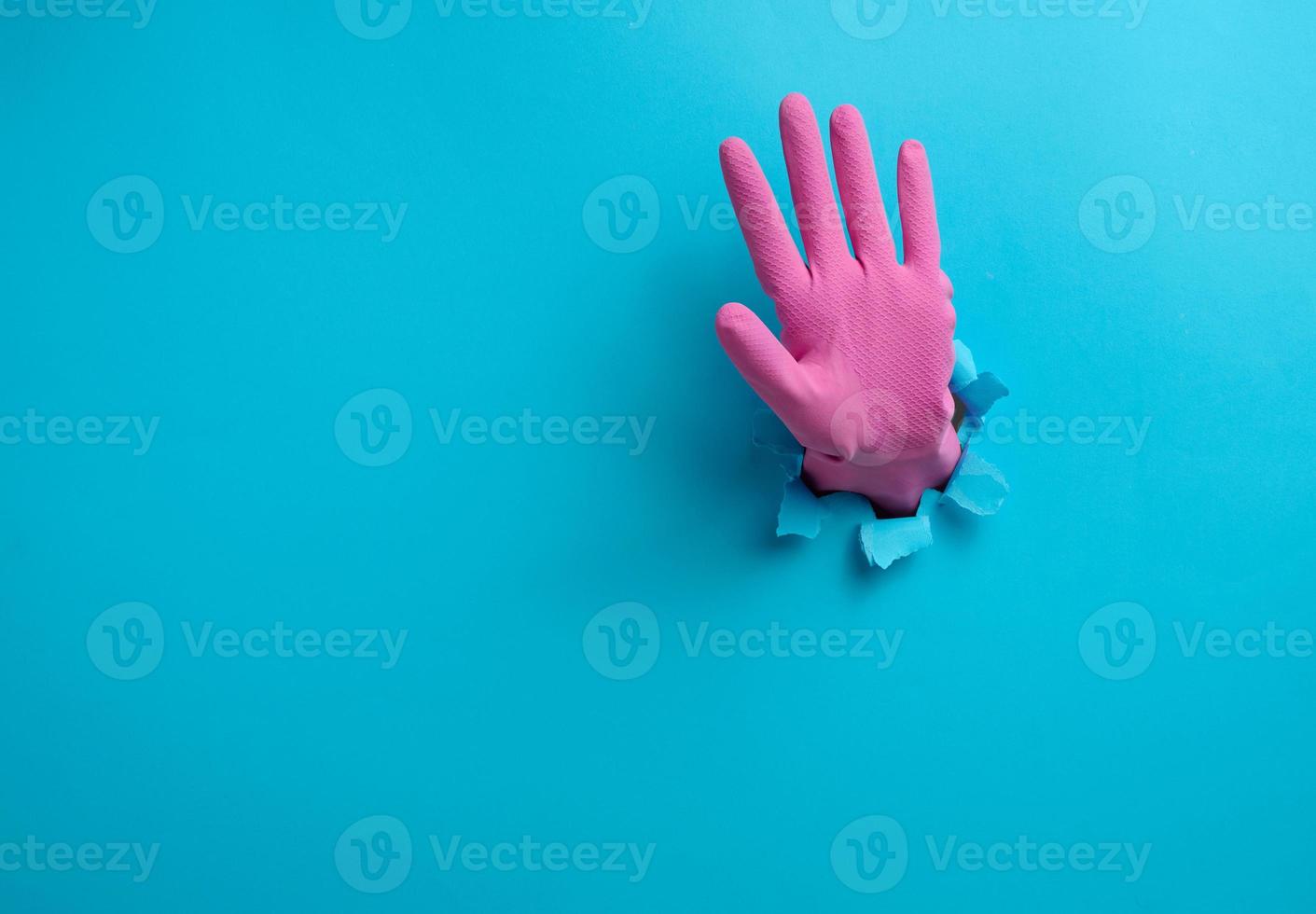 hand with an open palm sticks out of a torn hole in blue paper, gesturing to stop photo
