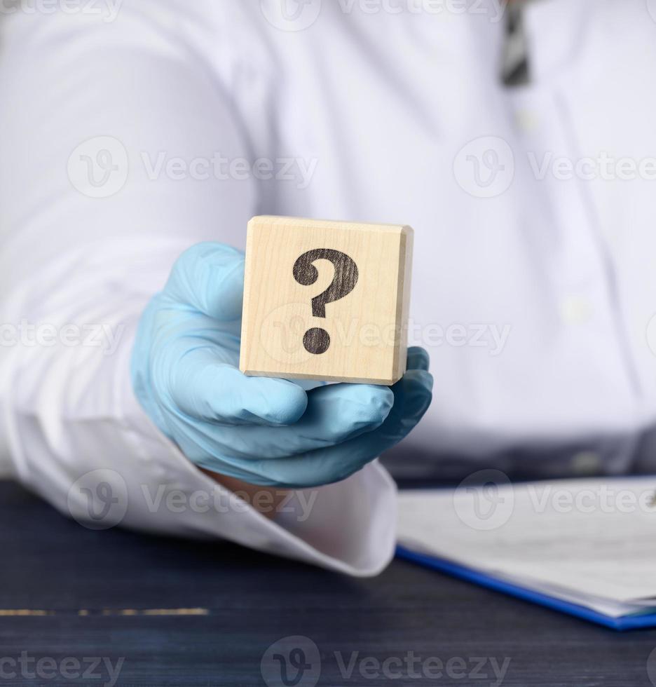 wooden cube with a question mark in the doctor's hand on a blue background. The concept of finding an answer to questions photo