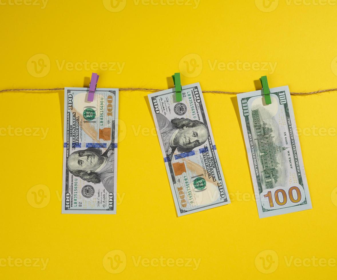 one hundred US dollar bills hang on a rope with clothespins, yellow background. Money laundering concept photo