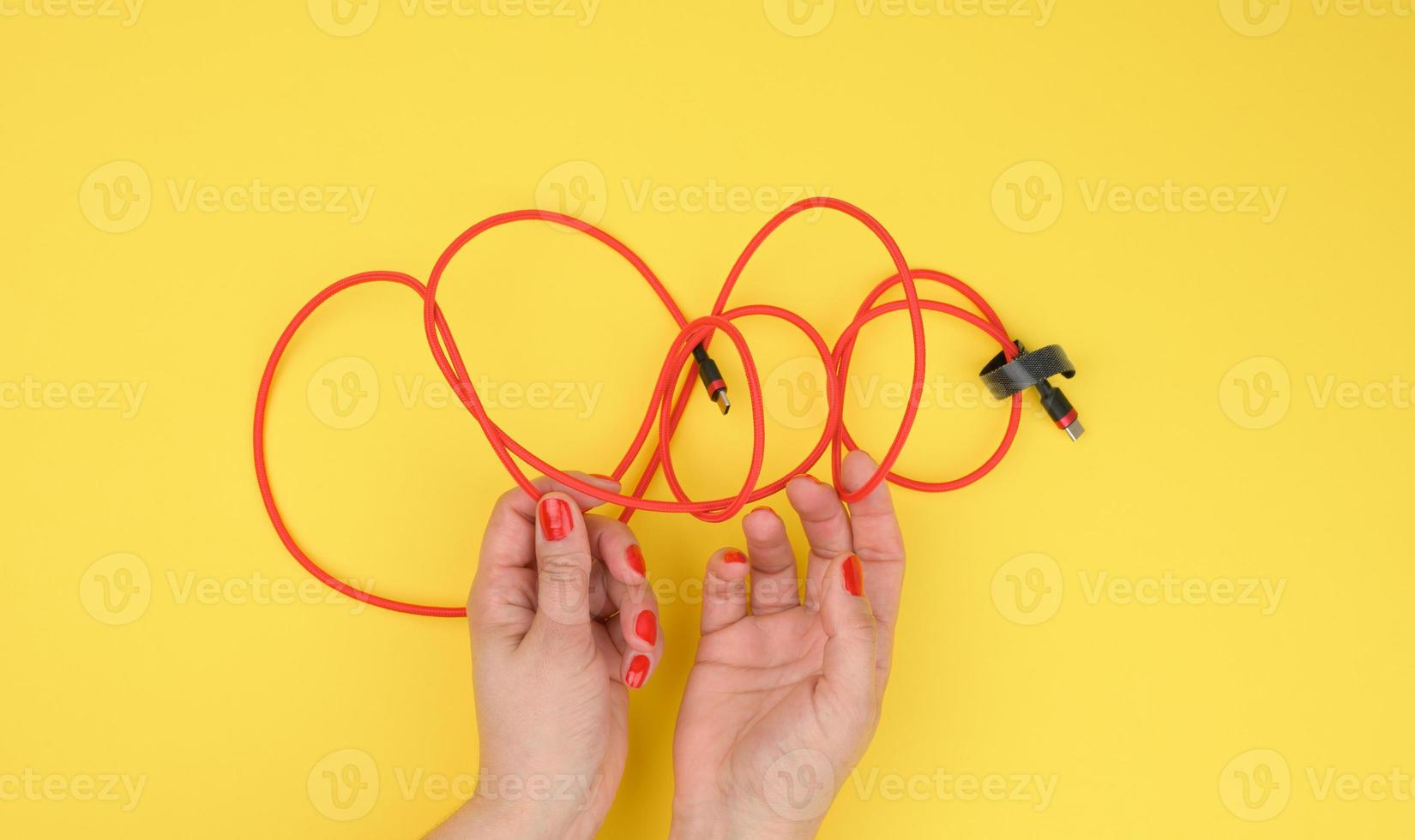 female hand holds twisted cable for charging mobile devices in a red textile wrapper on a yellow background photo