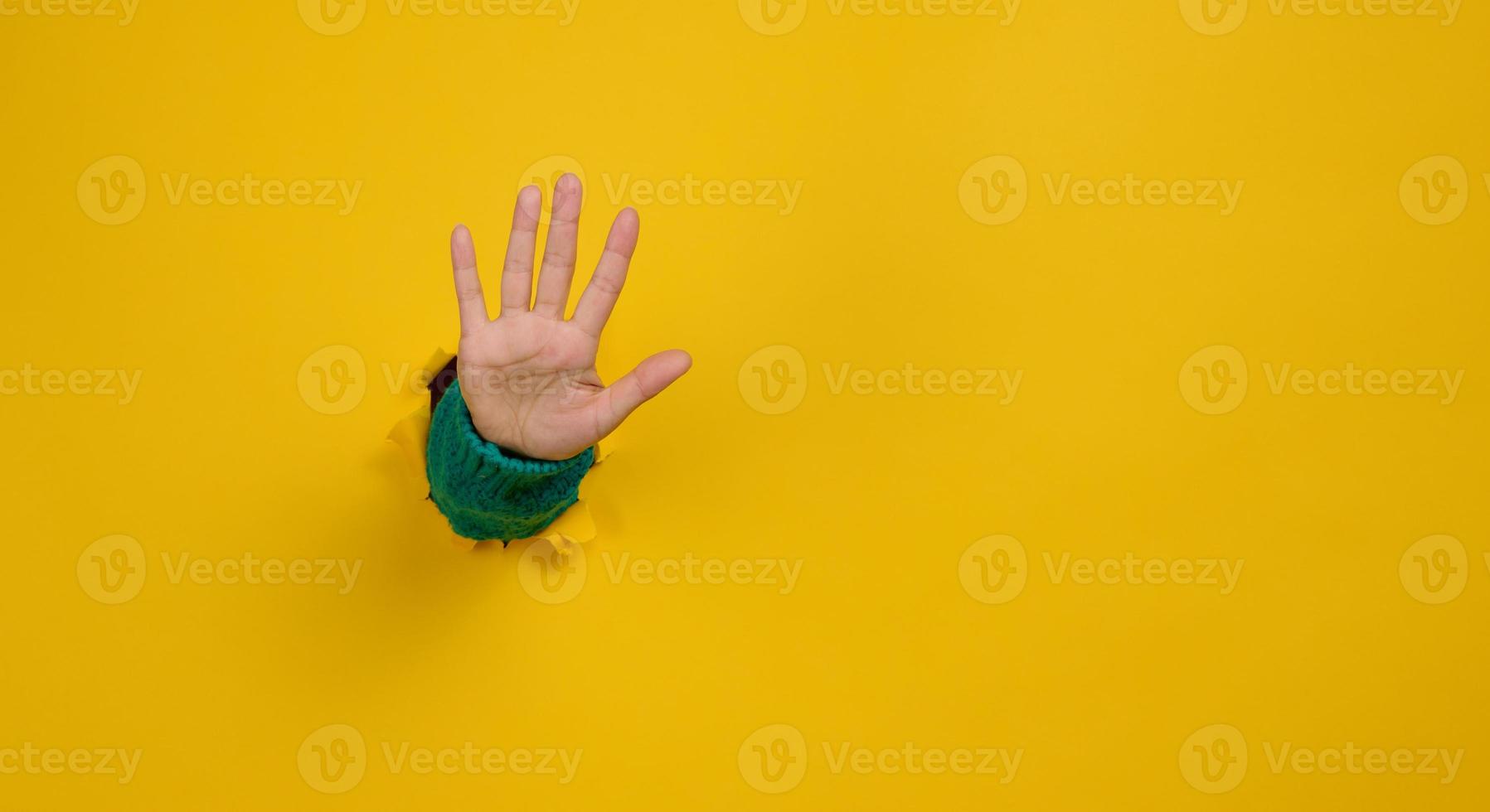 mujer mano con un abierto palma palos fuera de un Rasgado agujero en amarillo papel, gesticulando a detener foto