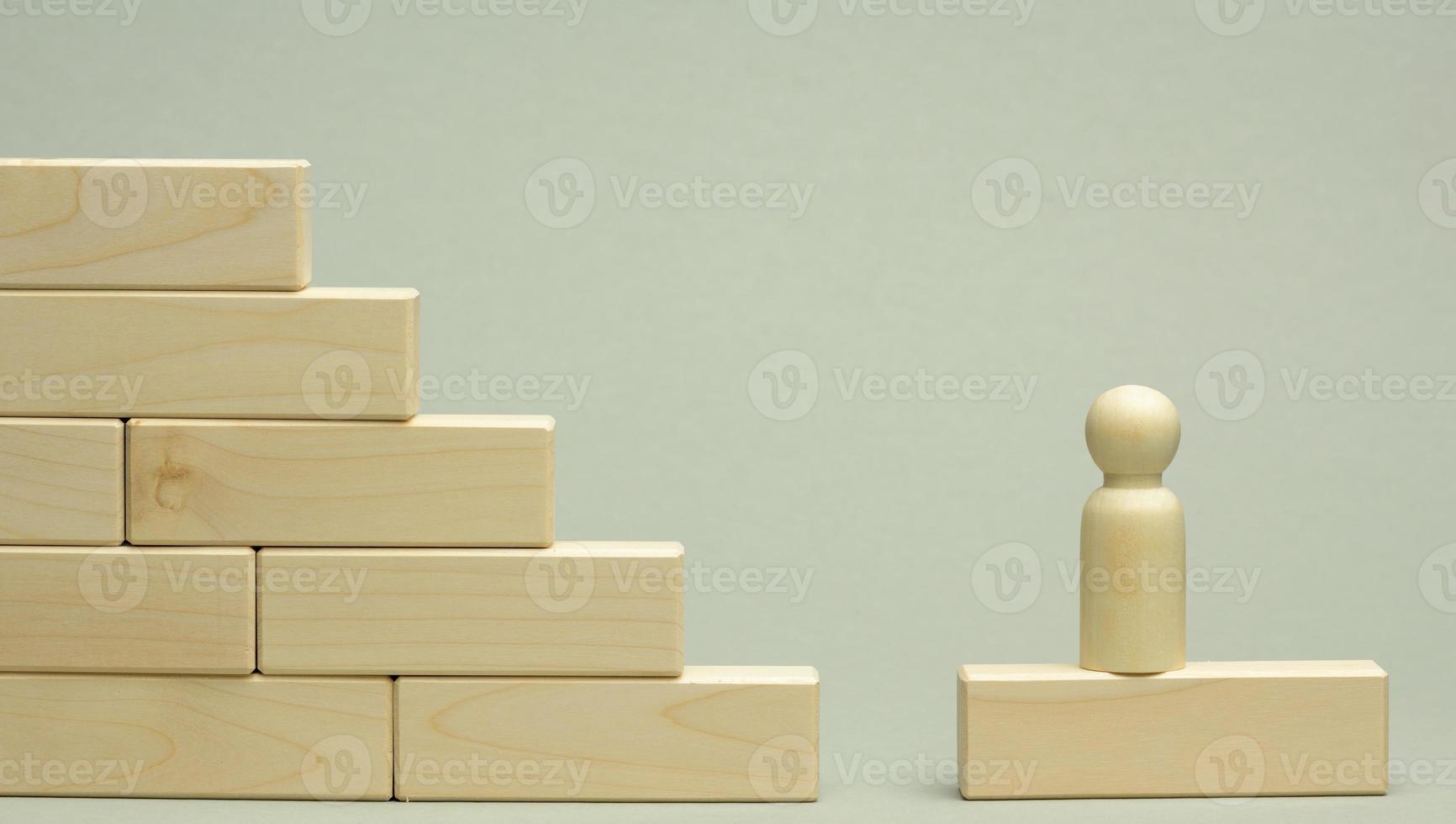 wooden figurine of a man stands on a staircase made of blocks on the first step photo