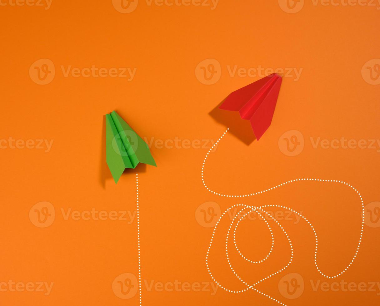 two paper airplanes with different trajectory of movement on an orange background photo