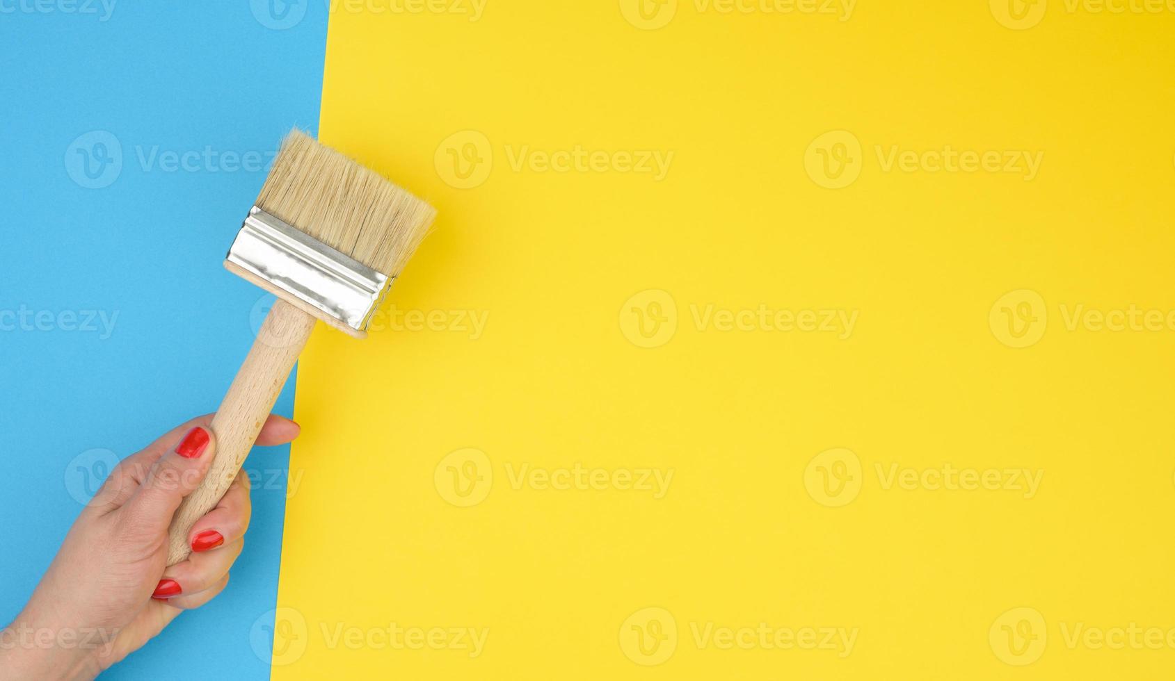 female hand hold new paint brush with wooden handle on a yellow background photo