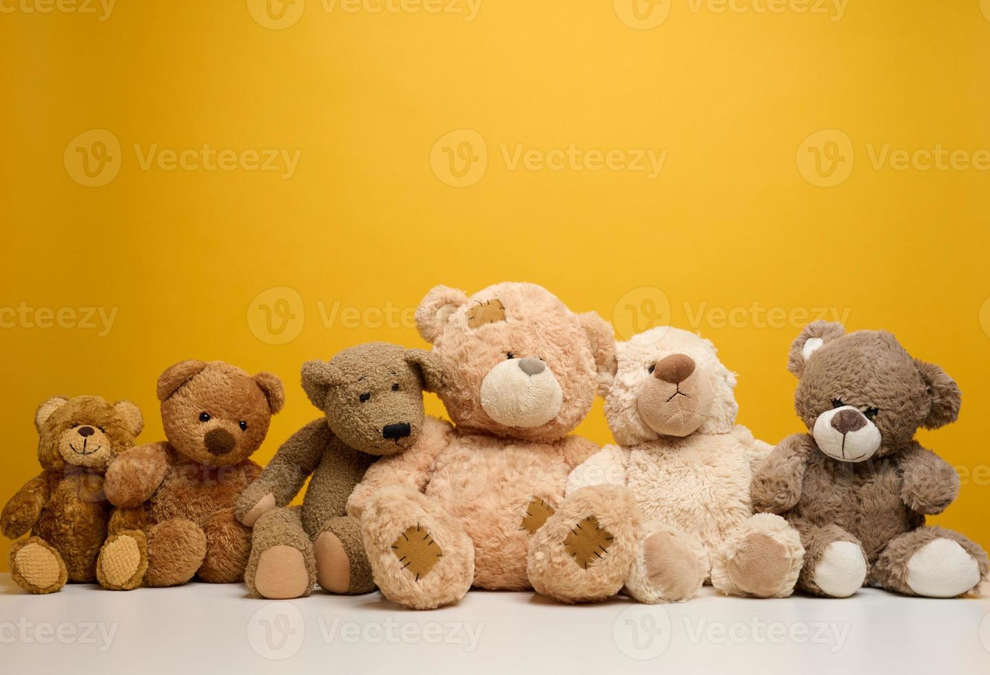 group of cute brown teddy bears sit on yellow background, childrens toy photo