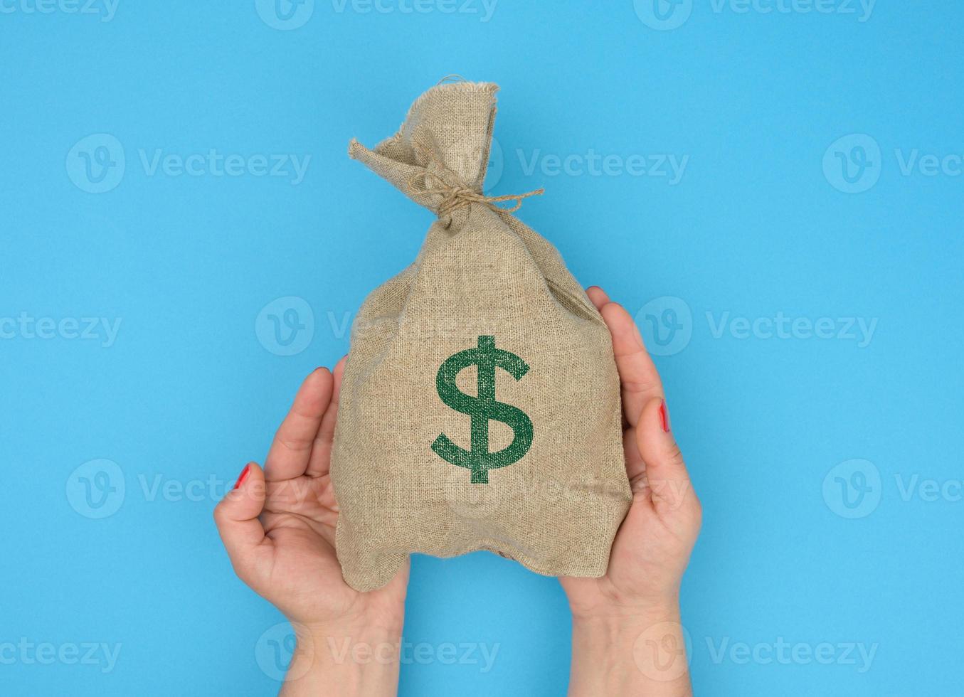 hand holds a canvas bag full of money with a US dollar icon on a blue background. Budget planning concept, profit and savings photo