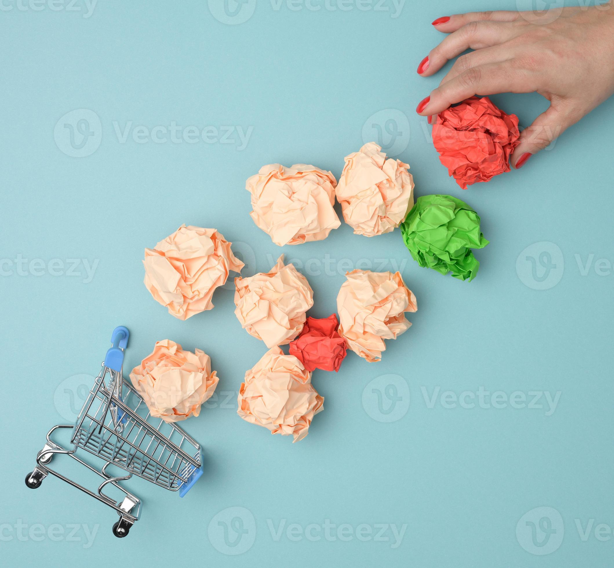 female hand throws crumpled paper balls into a miniature shopping cart