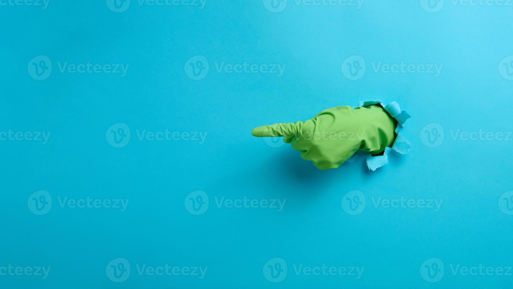 a hand in a green latex glove points a finger on a blue background. Place for inscription of discounts, offer or announcement. photo