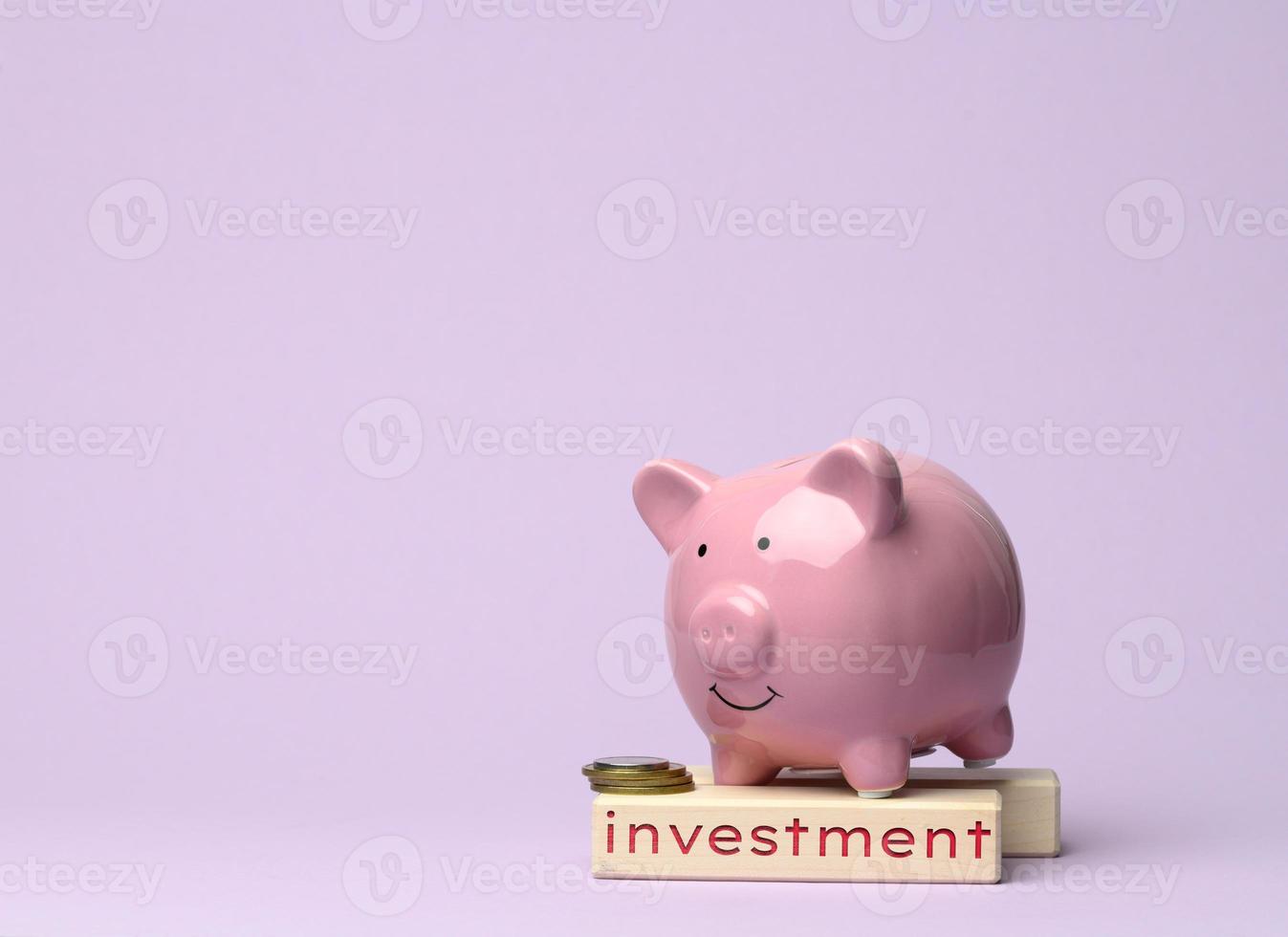 ceramic pink piggy bank and wooden cube with the inscription investment on a lilac background, concept of savings photo