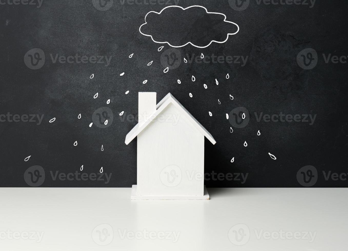 wooden house and a drawn cloud with rain with white chalk on a black chalk board. Real estate insurance concept photo