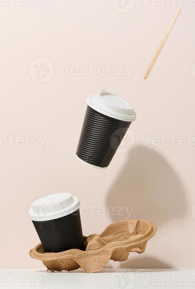 two brown cardboard cups with a white plastic lid. Disposable tableware levitates against a beige background photo