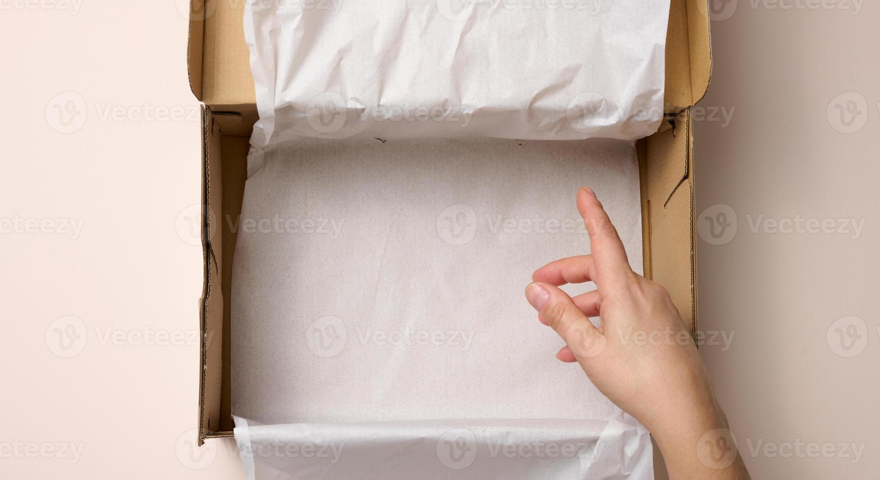 two female hands hold open paper box on a beige background, top view photo