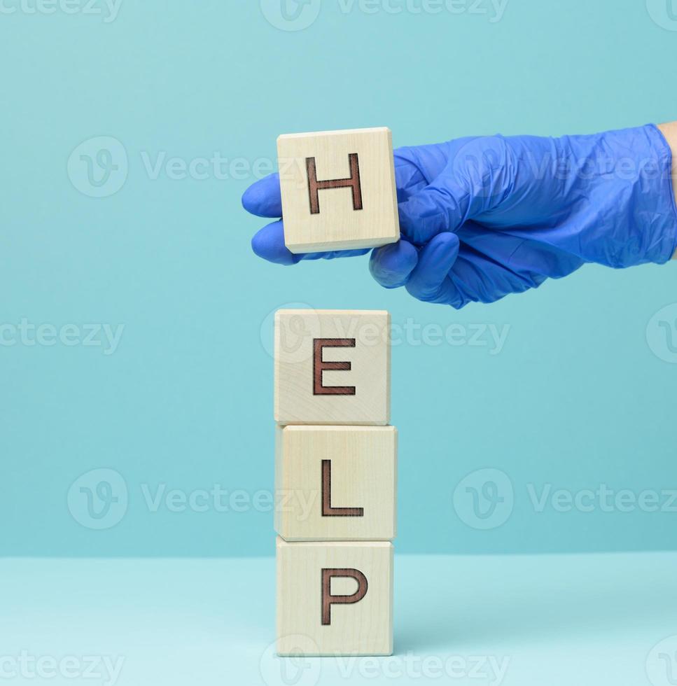 inscripción ayuda en de madera cubitos y un mano en un azul médico guante. primero ayuda concepto foto