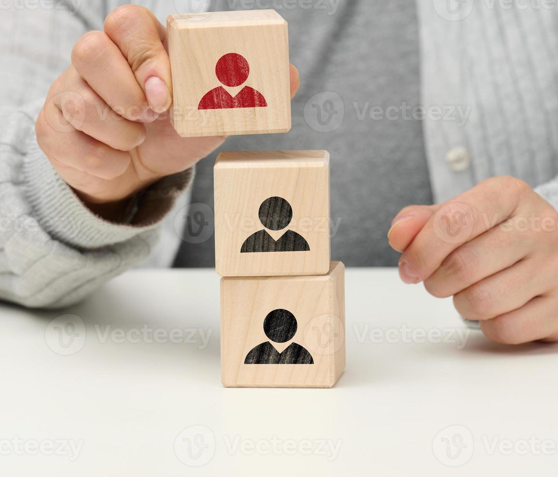 hembra mano sostiene un de madera cubo con un hombre. el concepto de hallazgo un líder, un talentoso empleado, jerarquía dentro el equipo foto