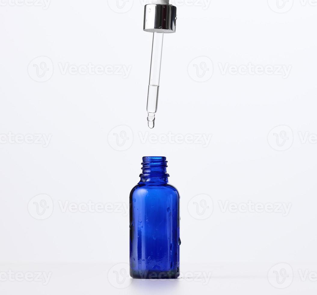 essential oil falling from the amber glass dropper. Blue bottle of cosmetic oil with a pipette photo