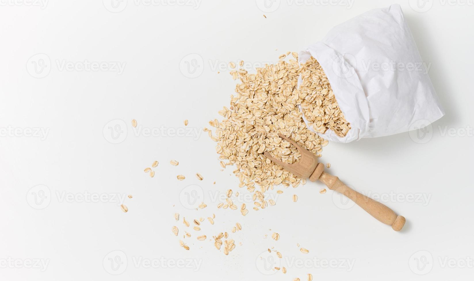 raw oatmeal in a white paper bag and a wooden spoon on a white table, breakfast porridge photo
