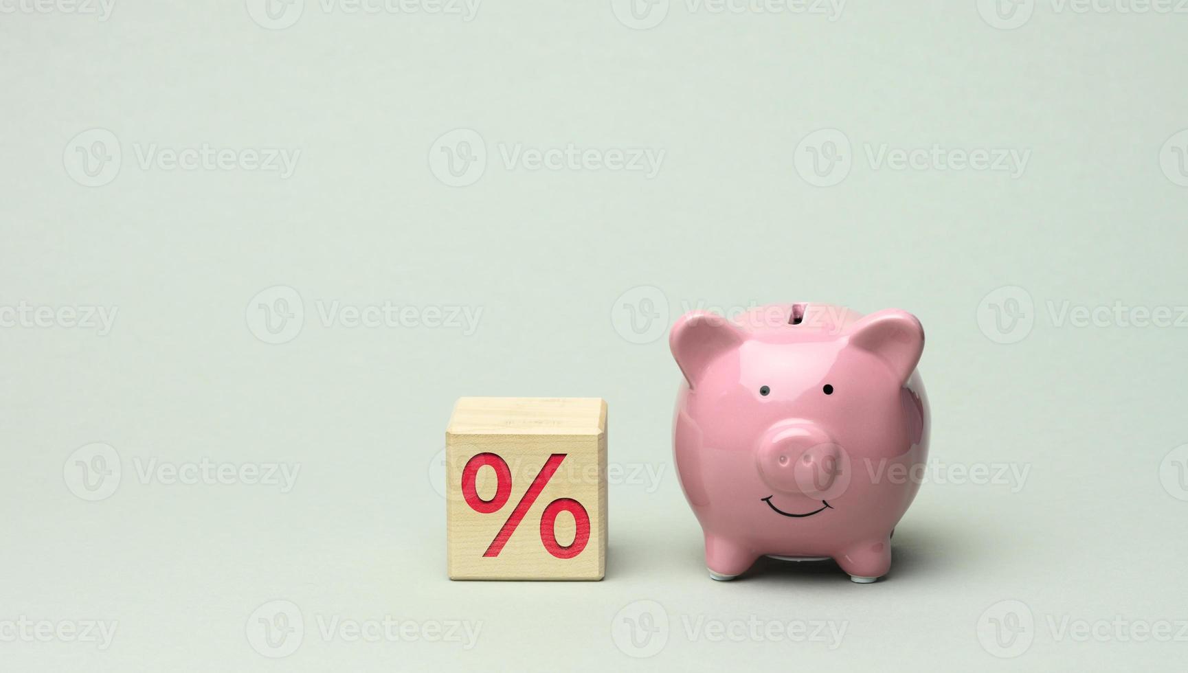 ceramic pink piggy bank and wooden cube with percent on gray background. Concept of increasing income from bank accounts photo