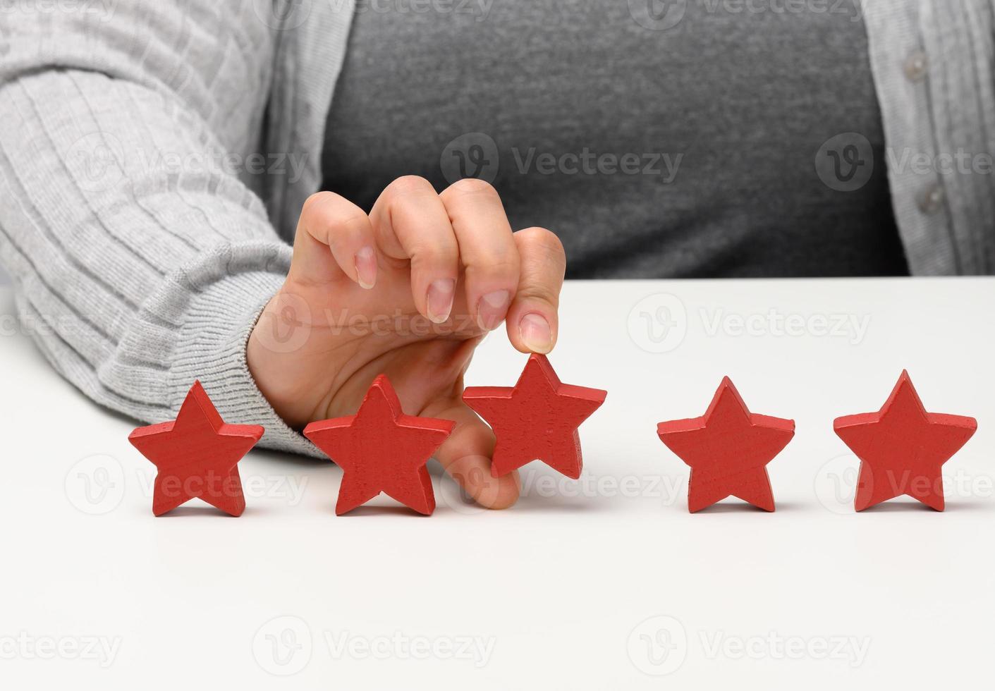 Customer experience feedback concept. Five red stars, the best rating of excellent services with a female hand to meet. White table photo