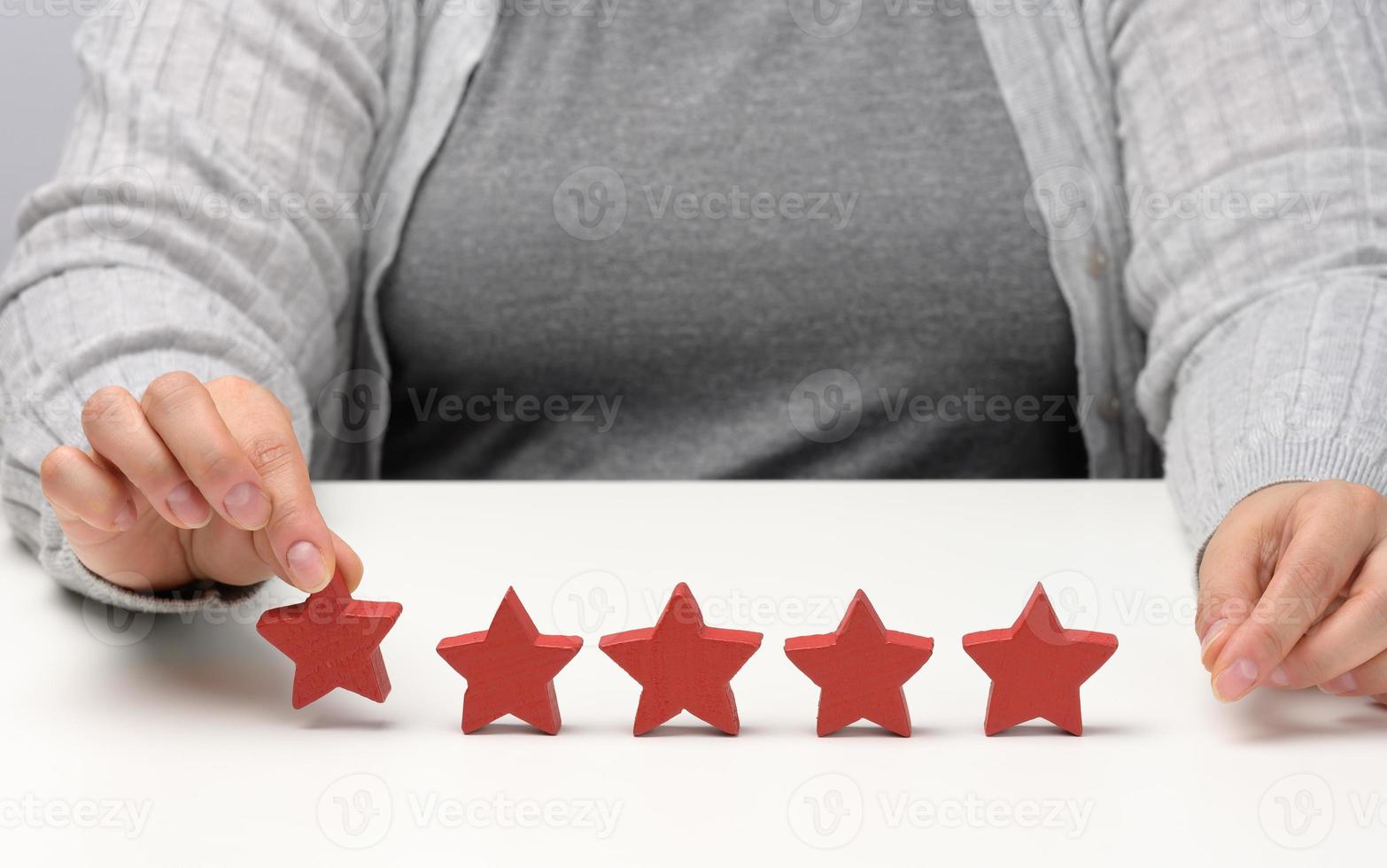 Customer experience feedback concept. Five red stars, the best rating of excellent services with a female hand to meet. White table photo