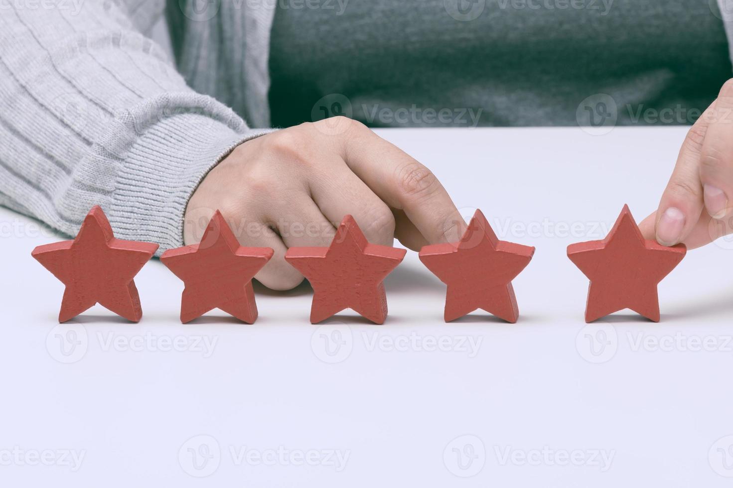 Customer experience feedback concept. Five red stars, the best rating of excellent services with a female hand to meet. White table photo