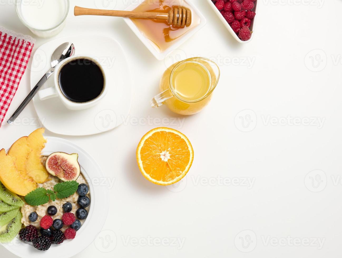 cup of black coffee, a plate of oatmeal and fruit, honey and a glass of milk on a white table photo