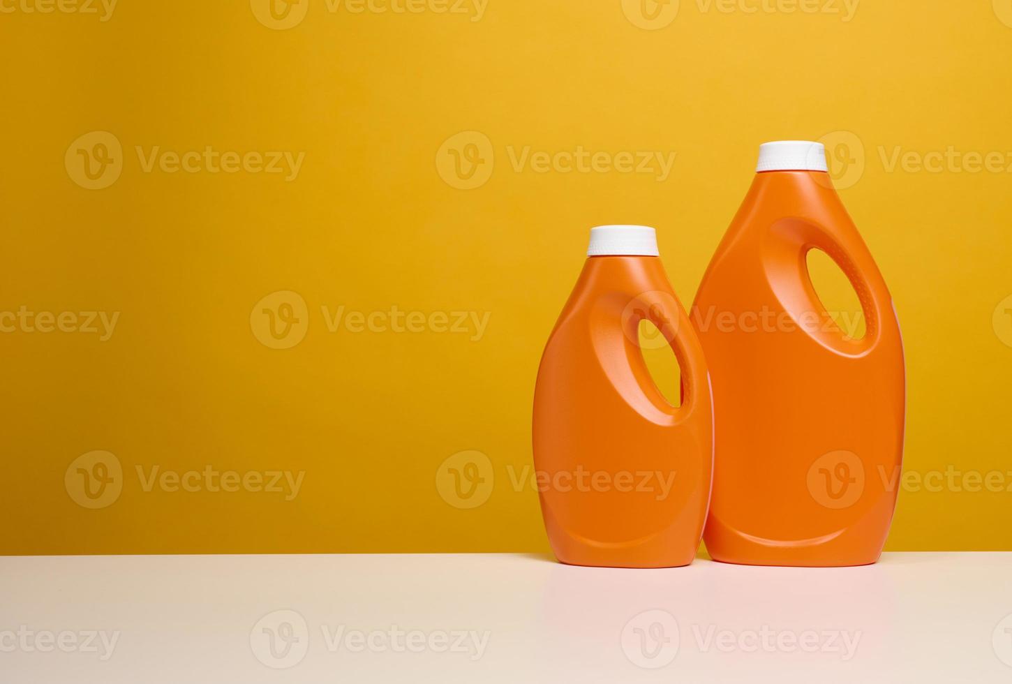 two plastic orange bottles with liquid detergent stand on a white table, yellow background photo