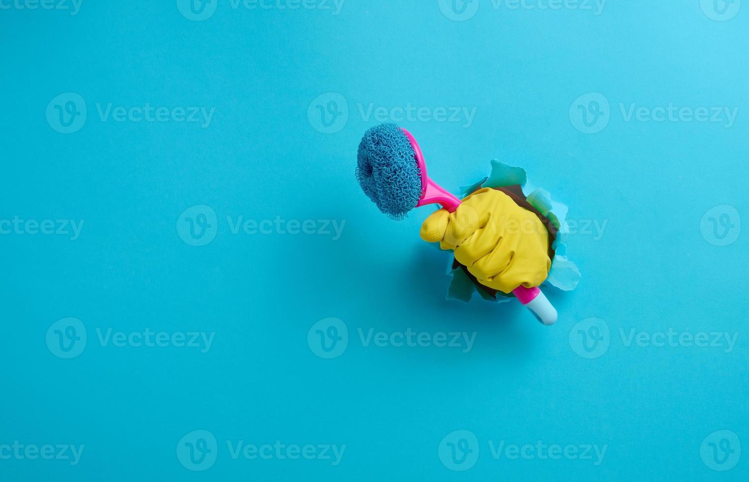 hand in a yellow rubber glove holds a plastic cleaning brush on a blue background photo