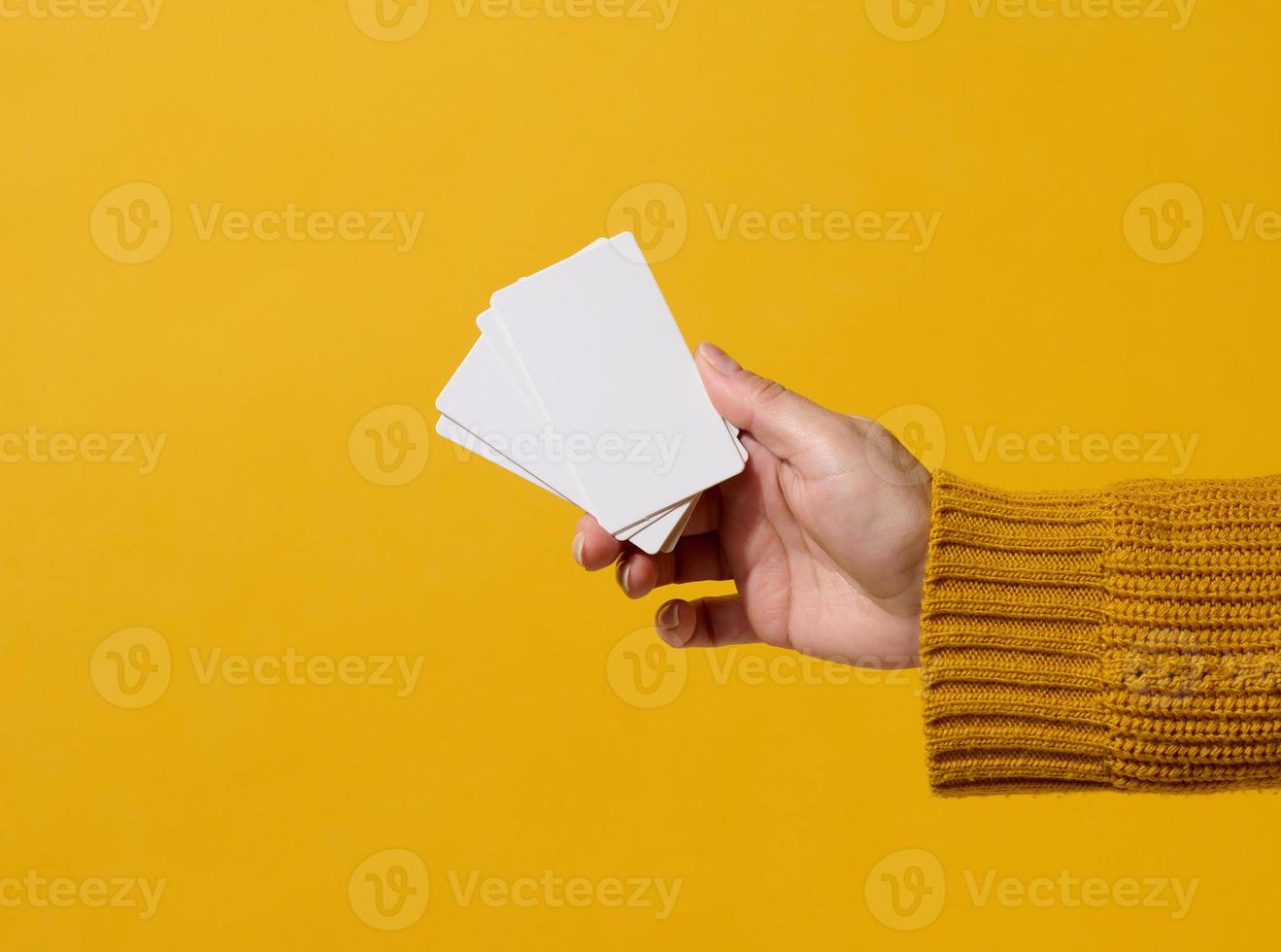 Female hand holding empty paper white business card on a yellow background. Copy space photo