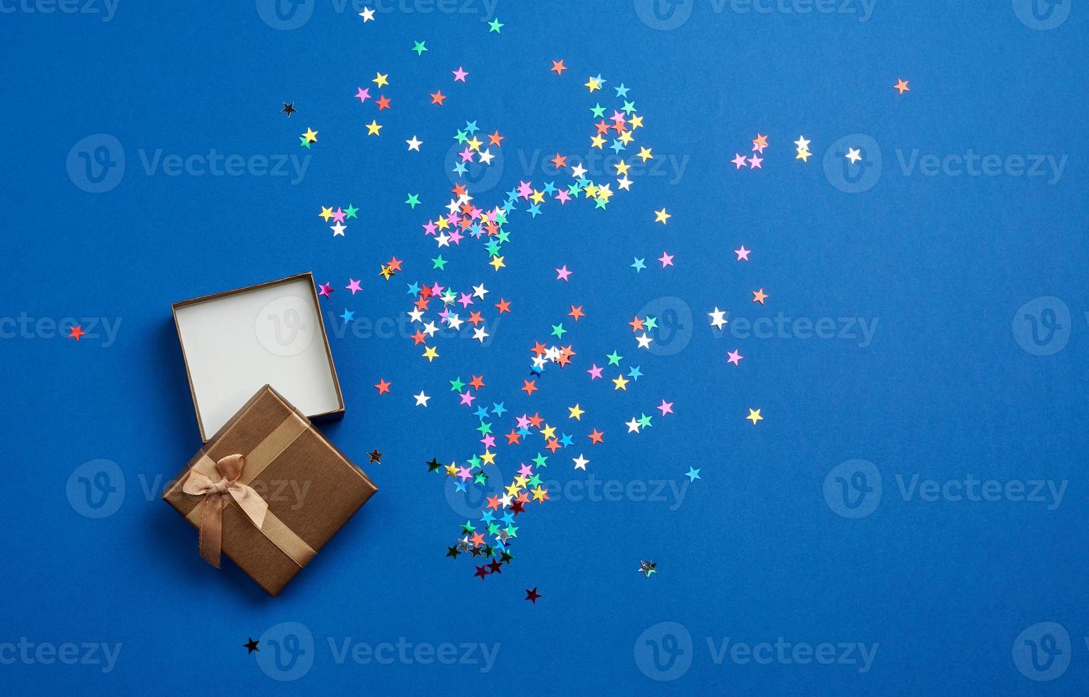 open square empty gift box on a blue background, near multi-colored sequins photo