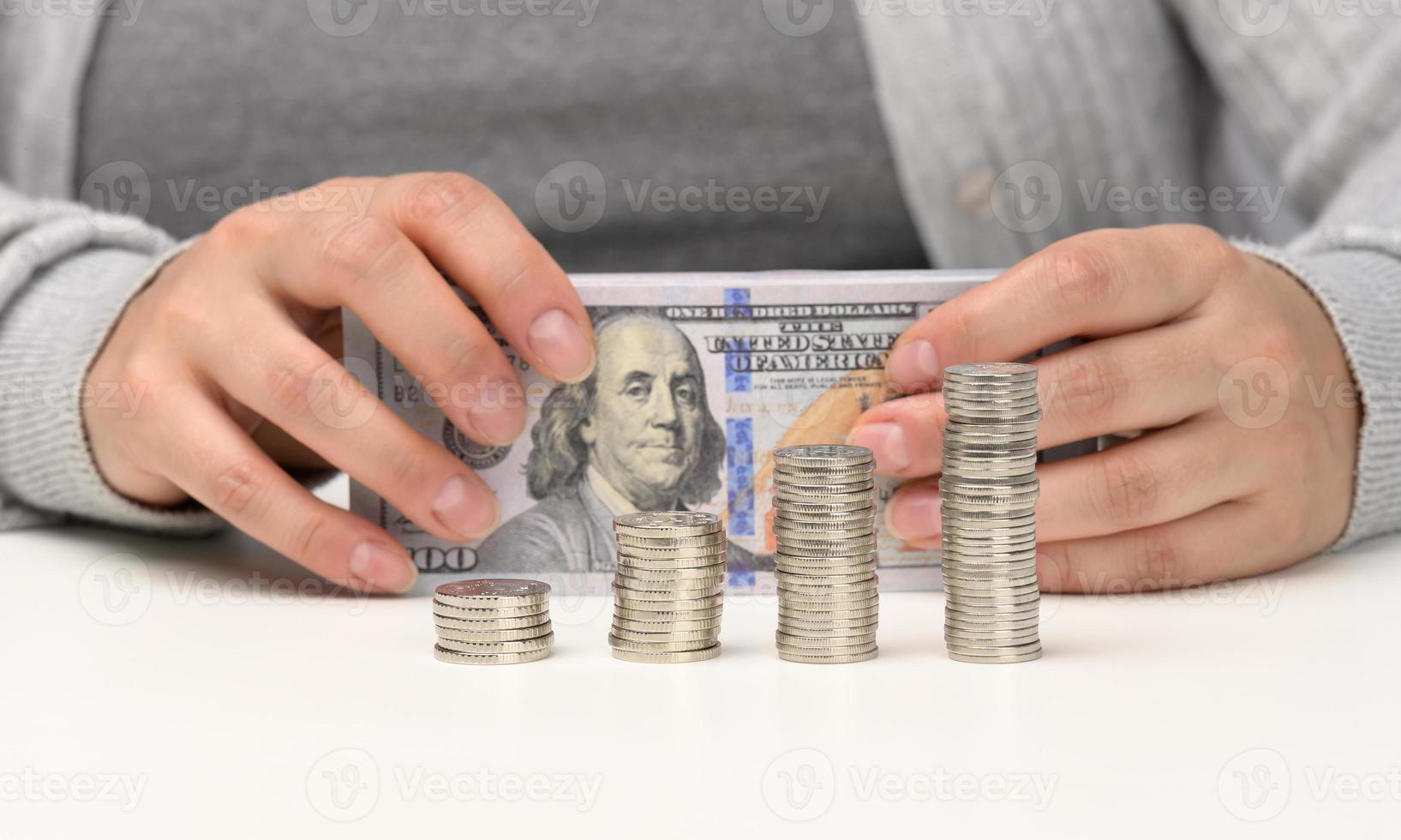 stack of coins on white chtoli and female hands are holding a stack of paper American dollars. The concept of budget control, accumulation, profit making photo