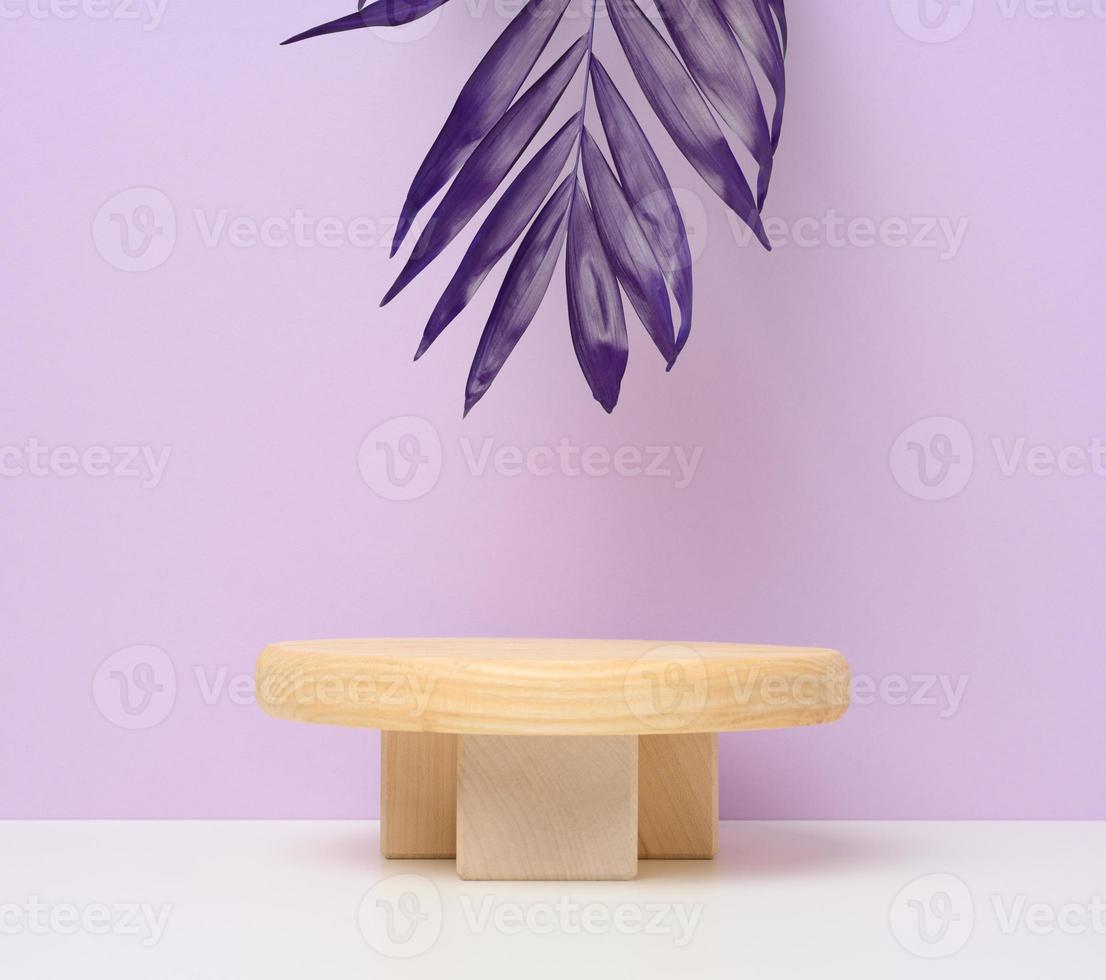 Stage for displaying products, cosmetics with a round wooden podium and a palm leaf. Purple paper background photo