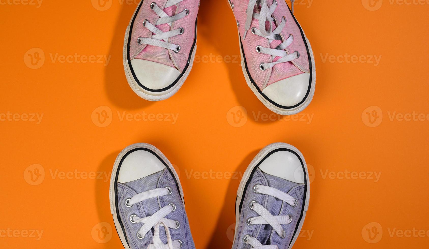 two pairs of textile sneakers on an orange background stand opposite each other. Dialogue and confrontation concept photo