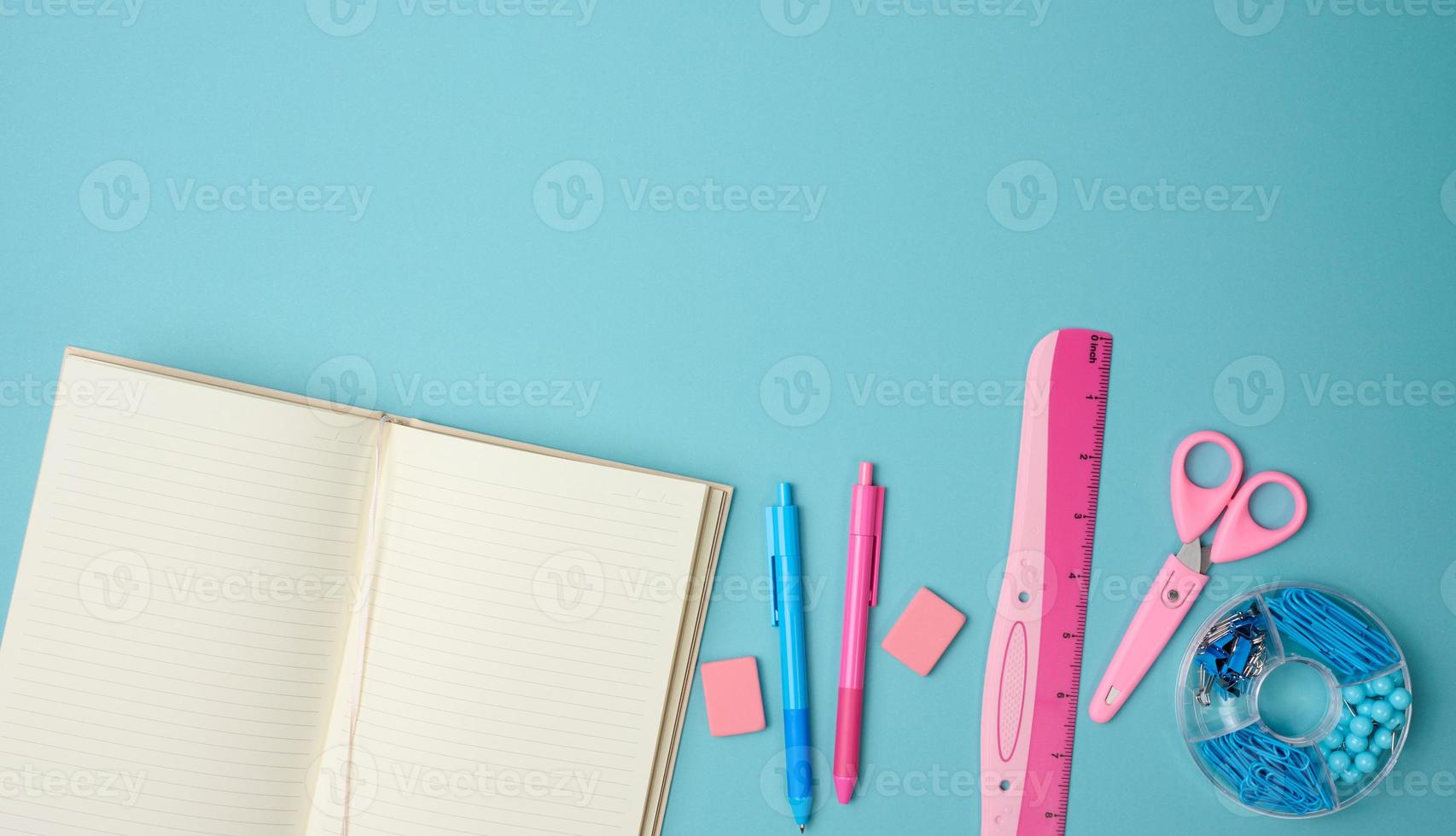 open notebook with blank pink sheets, scissors and ruler on blue background, top view photo