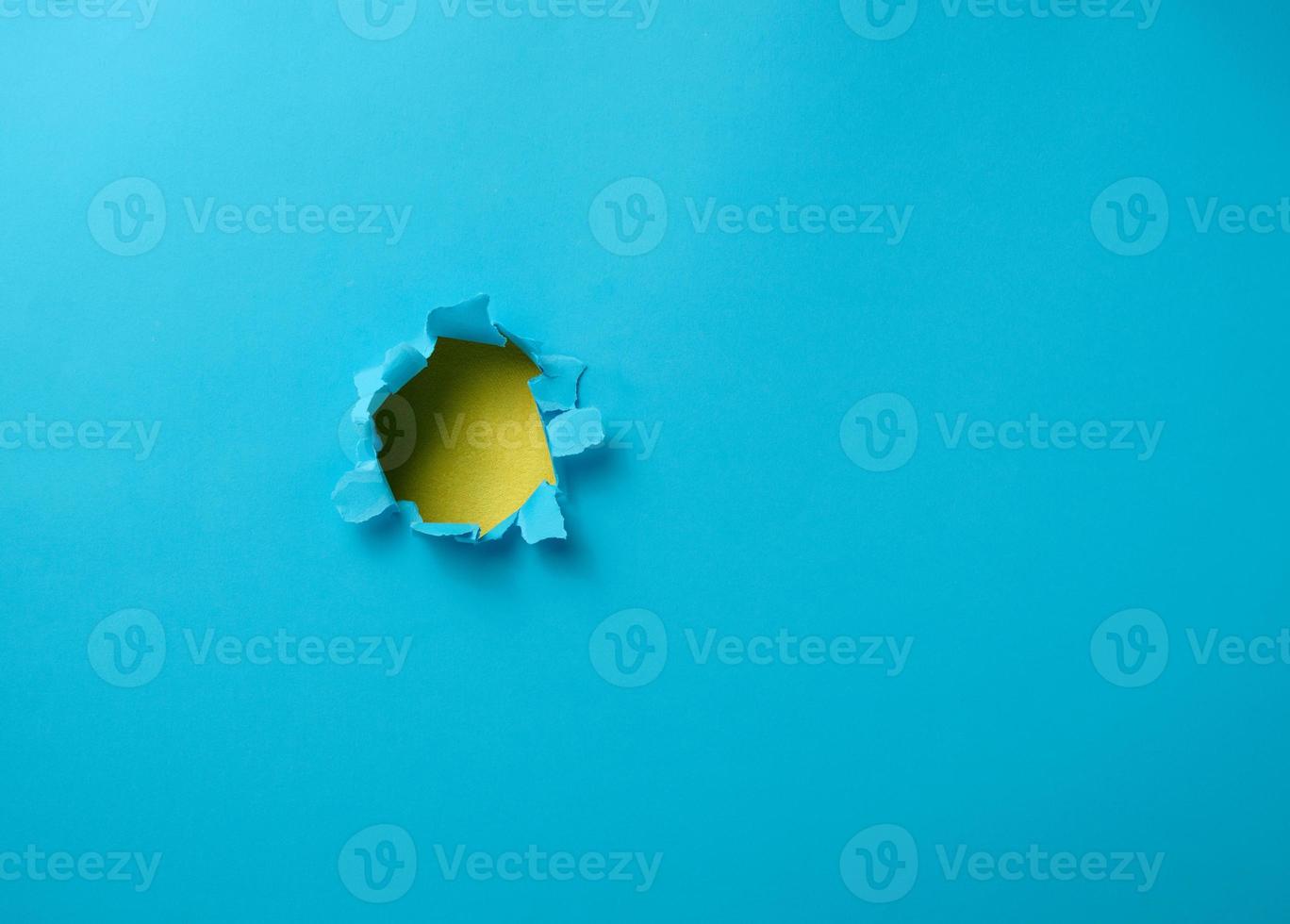 hole with torn edges in blue paper, full frame photo