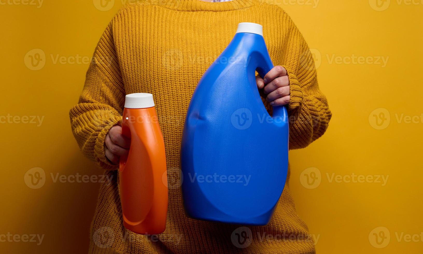 woman in a knitted sweater holds an orange  and blue plastic bottles with liquid washing gel. Laundry and chores, yellow background photo