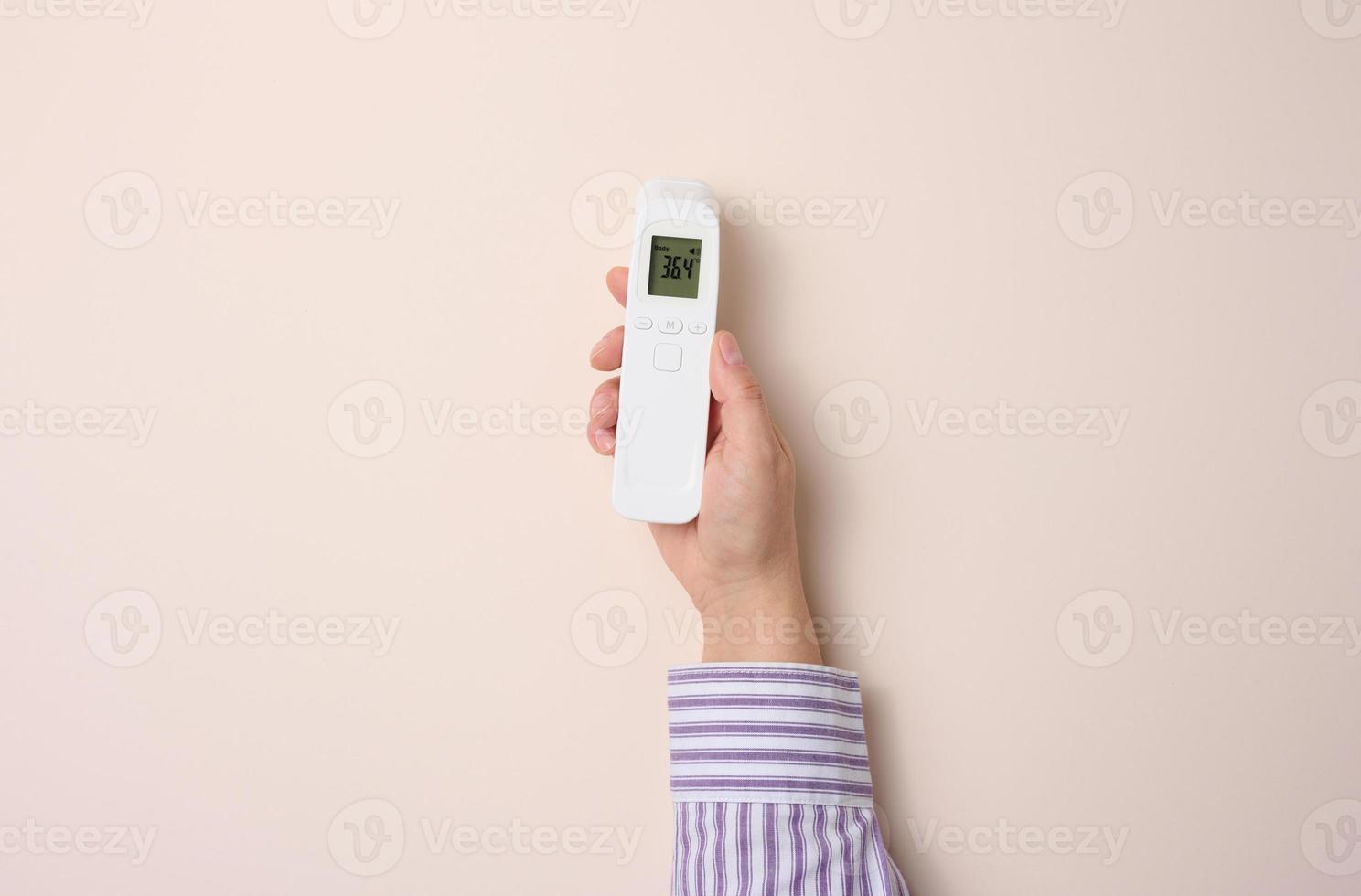 female hand holding a plastic non-contact thermometer on a beige background photo