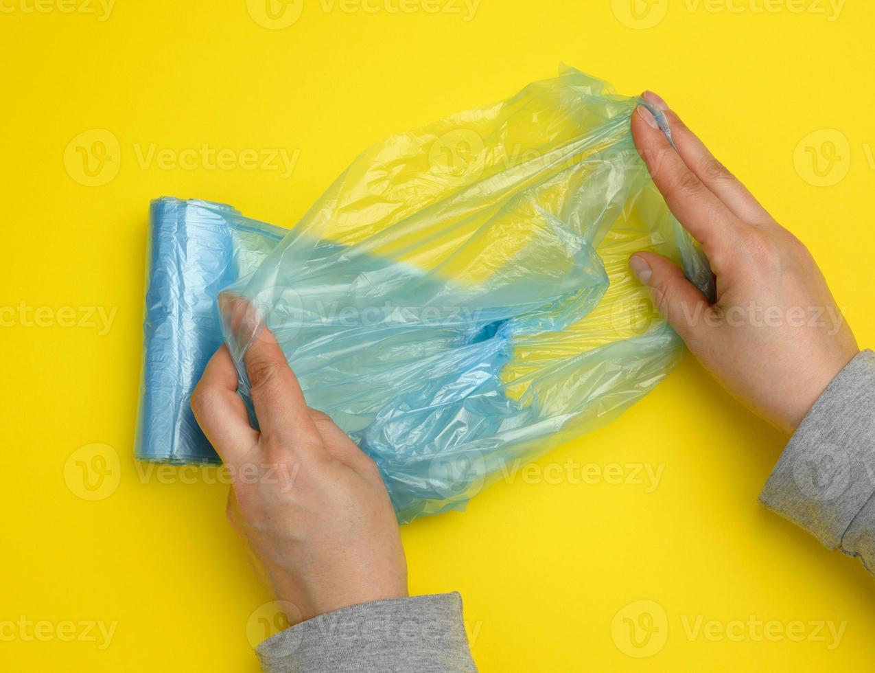 mano femenina desenrolla una bolsa de plástico azul para basura, fondo amarillo foto