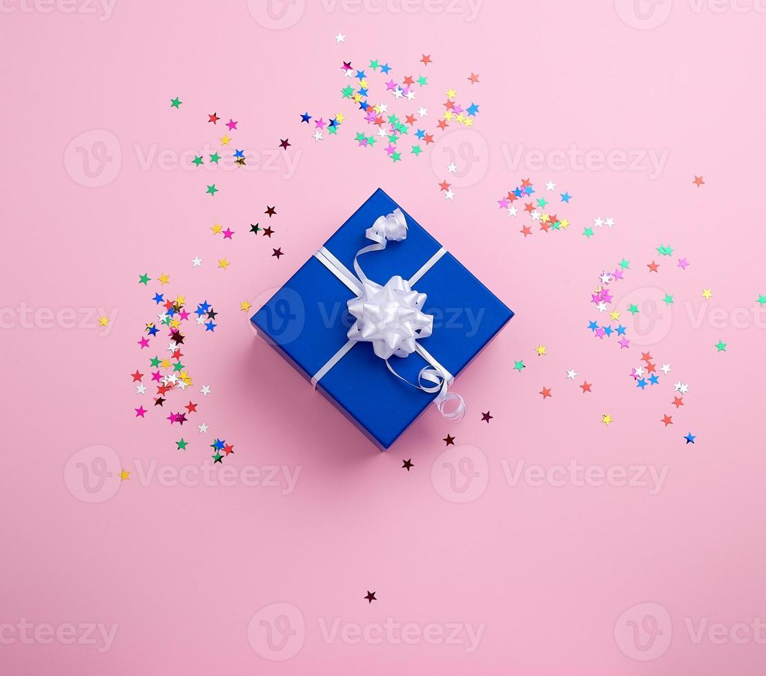 beautiful blue closed box with white bow on a pink background with multi-colored sparkles photo